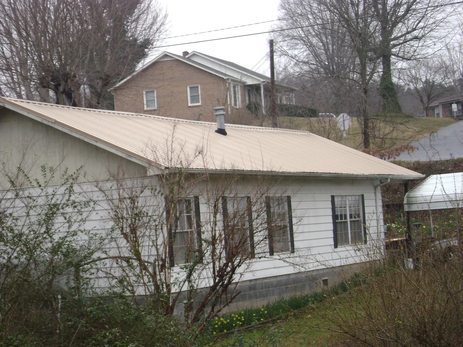Tan metal roof on a white sided house set into a hillside — Commercial Roofing by Roofing Brothers in Oak Harbor